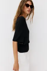 Top de punto color beige con cuello barco y mangas cortas anchas tipo murciélago. Cuenta con cintura entallada con ribete elástico y un cinturón fino de cuero sintético marrón con hebilla metálica dorada.