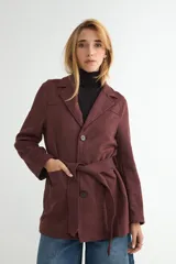 Chaqueta de gamuza sintética color bordó, con cuello solapa, cierre frontal de botones y cinturón ajustable del mismo material. Posee bolsillos frontales y mangas largas.
