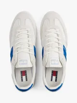 Zapatillas deportivas de estilo vintage Tommy Jeans modelo The Greenwich, confeccionadas en ante color blanco con paneles laterales en azul vibrante y detalles en gamuza gris claro. Presentan cierre con cordones, suela cupsole de goma y logo de la marca en el lateral.