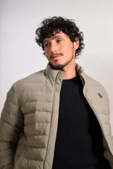 Campera puffer color beige con cierre frontal, cuello alto y logo de la marca bordado en el pecho.