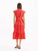 Vestido camisero largo color rojo, de mangas cortas con hombros estructurados y falda escalonada con volados. Presenta cierre frontal con botones y lazo ajustable en la cintura del mismo material.