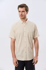 Camisa de manga corta confeccionada en mezcla de lino y algodón, color beige, con cuello camisero abotonado, bolsillo frontal en el pecho y cierre de botones.