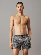 Short de baño negro con estampado de líneas onduladas blancas. Cuenta con cintura elástica ajustable con cordón, bolsillos laterales y trasero, forro de malla y logo de Calvin Klein en el bajo.