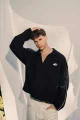 Buzo tipo polo de manga larga, color negro, con cuello y cierre parcial frontal. Presenta un pequeño bordado en el frente y la espalda.