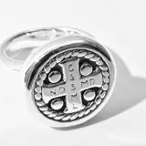 Anillo plateado con forma circular y diseño de cruz en el centro.