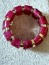 Brazalete elástico de diseño protagonista, compuesto por piezas rectangulares de acrílico en tono fucsia con efecto marmolado, intercaladas con eslabones metálicos dorados.