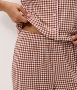 Pijama largo de dos piezas confeccionado en ribana con estampado de cuadros vichy en tonos marrón y blanco. Incluye una blusa de manga corta con cuello solapa, cierre frontal de botones y detalles de vivo contrastante, y un pantalón de pierna recta con cintura elástica.