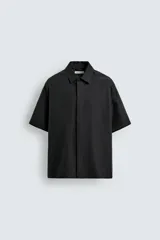 Camisa de manga corta con corte relajado, confeccionada en tejido fluido con mezcla de lyocell. Presenta cuello solapa, cierre frontal con botonadura oculta por solapa y aberturas laterales en el bajo.