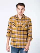 Camisa de franela a cuadros en tonos mostaza, negro y blanco, con bolsillos frontales con solapa y botones.
