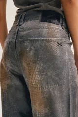Jean de corte amplio en toda la pierna, con textura desgastada y efecto animal print de serpiente o cocodrilo en tonos gris y terracota.