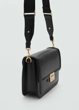 Bolso bandolera de tamaño mediano en color negro, con diseño estructurado y cierre de solapa con broche metálico dorado. Cuenta con doble compartimento interior, forro textil y asa larga extraíble.