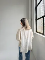 Camisa beige de lino de corte holgado, con cuello mao, mangas largas con puños fruncidos y cierre frontal de botones.