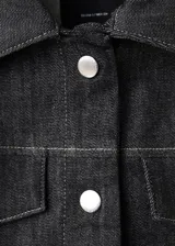 Chaqueta de denim en color negro, de corte clásico con cierre frontal de botones metálicos, cuello camisero y bolsillos con solapa en el pecho.