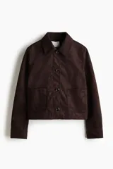 Chaqueta corta marrón de acabado cepillado suave tipo gamuza, con cuello clásico, cierre frontal de botones, dos bolsillos de parche delanteros y mangas largas.