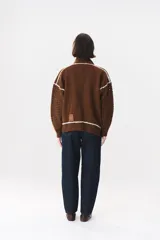 Campera de tejido de punto color marrón con destellos de lurex, corte oversize y cierre frontal. Presenta detalles de costuras y terminaciones en color crema, cuello alto y bolsillos frontales.