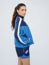 Campera deportiva Umbro del Club Nacional de Football, modelo Sky para mujer. Diseño en tonos azul marino y celeste con detalles en blanco y líneas finas rosadas, cuello alto, cierre frontal y bolsillos.