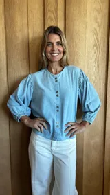 Camisa de jean celeste con cuello redondo, mangas abullonadas y puños elásticos. Cierre frontal con botones.