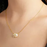 Collar de cadena fina dorada con dije de flor que presenta un pétalo con incrustaciones de cristales brillantes y otro pétalo con acabado de nácar.