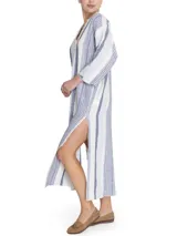 Túnica de corte amplio confeccionada en una mezcla de lino y algodón orgánico, con diseño a rayas verticales en tonos azul y blanco. Presenta escote en V con detalle desflecado, mangas tres cuartos y aberturas laterales en el ruedo.