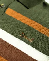 Buzo tejido de punto con diseño de rayas horizontales en tonos verde, marrón y blanco. Presenta cuello tipo polo con cierre de tres botones, mangas largas con puños acanalados y logo de la marca bordado en el pecho. Incluye una etiqueta decorativa en la parte inferior.