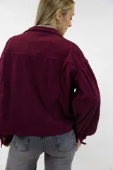 Campera corta de pana color beige, con cuello clásico, cierre frontal con botones y amplios bolsillos con solapa en el pecho. Cuenta con mangas largas abullonadas y diseño holgado.