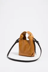 Bolso de hombro Bimba y Lola tamaño mini, de estructura blanda y color marrón oscuro, confeccionado en piel vacuna. Presenta asas de mano de piel y una correa extraíble, con detalles metálicos y logo de la marca en el frente.