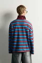 Polo de manga larga con diseño de rayas horizontales en tonos bordó, celeste y blanco, de corte relaxed fit, con cuello tipo polo y cierre frontal de botones.
