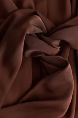 Vestido midi camisero de sarga liviana con brillo satinado, color marrón, de manga larga, con hombros caídos, botonadura frontal y puños sencillos. Presenta paneles drapeados cruzados en la cintura con tiras para atar al costado.