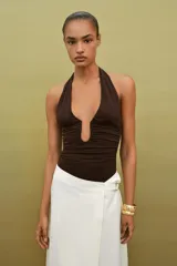 Body de cuello halter con espalda descubierta, confeccionado en poliamida. Presenta un diseño drapeado en los laterales y una abertura frontal con detalle metálico. Posee cierre con botones a presión en la parte inferior y lazada en el cuello.