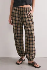 Pantalón baggy de tiro medio con estampado a cuadros en tonos beige, tostado y negro, confeccionado en algodón peinado. Presenta cintura elástica con cordón de ajuste y puños elastizados en los tobillos.