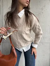 Sweater de punto color beige con diseño floral en relieve, cuello redondo y mangas largas. Presenta puños y ruedo acanalados.