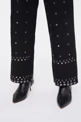 Pantalón negro de corte carrot, con bolsillos laterales, cierre frontal y aplicación de tachas metálicas en toda la prenda y en los dobladillos.
