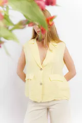 Chaleco sastrero de lino color amarillo pastel, con cuello solapa, cierre frontal con botones y bolsillos decorativos con solapa en la parte inferior.