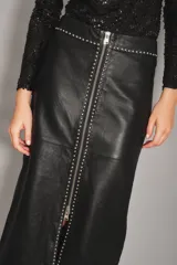 Falda midi de cuero ovino color negro, con diseño de tiro alto y cierre frontal completo con cremallera metálica. Presenta detalles de tachas decorativas a lo largo de la costura central y el borde del cierre.