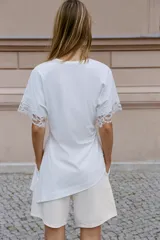 Camiseta negra de algodón con cuello redondo, manga corta y detalle de aplicación de encaje a tono en los puños. Presenta un diseño con bajo asimétrico y frunce lateral.