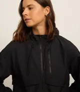 Campera deportiva cortaviento color blanco, con capucha ajustable, cierre frontal por cremallera y diseño de corte holgado. Incluye saquito para guardar.