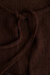 Top corto sin mangas de punto marrón oscuro, con escote redondo y abertura frontal que se cierra con tres lazos anudados. Presenta un ruedo con volado (peplum).