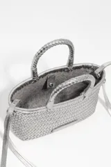 Minibolso estructurado de cuero trenzado color plateado, con asas de mano y correa larga de hombro ajustable. Incluye una pequeña etiqueta de cuero con logotipo grabado en la parte frontal.