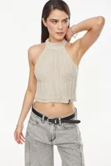 Top de punto estilo halter, color crudo, con cuello alto ajustado, diseño sin mangas y corte corto.