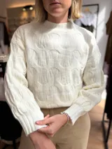 Sweater de punto color blanco con cuello alto y diseño de textura en relieve. Presenta mangas largas con puños acanalados y un corte holgado.