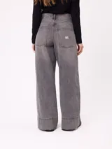 Jean de corte wide leg con diseño de pata ancha y costuras laterales visibles. Presenta un lavado azul clásico con efecto desgastado y cierre frontal con botón y cremallera.