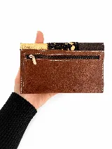 Billetera de cuero de diseño combinado en tonos chocolate, negro y champagne, con textura tipo animal print en el centro y placa metálica con el logo de la marca.