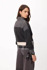 Sweater de punto con diseño patchwork en tonos gris, grafito y crudo, con cuello alto tejido. Presenta una estructura de bloques de color y texturas variadas, incluyendo detalles de trenzas y tejido acanalado.