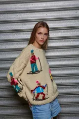 Sweater tejido de lana color beige con cuello redondo y mangas largas. Presenta bordados de figuras esquiando en distintos colores.