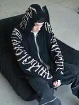 Hoodie con cierre frontal, confeccionado en tejido de punto 100% algodón. Es una prenda reversible con diseño de estampado gráfico en mangas y capucha, y presenta detalles de roturas intencionales en puños, ruedo y bolsillos.