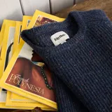 Buzo de punto con cuello redondo y diseño jaspeado en tonos azules con motas multicolores. Presenta una textura acanalada y corte clásico.