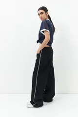 Pantalón de jean ancho color negro, de tiro bajo y confeccionado en algodón. Cuenta con una línea bordada color marrón en ambas piernas y cinco bolsillos.