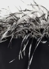 Vestido corto negro de corte entallado y escote palabra de honor, decorado con plumas de avestruz en el borde superior. Incluye tirantes desmontables y cierre lateral con cremallera.