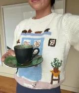 Sweater de punto color blanco marfil con diseño jacquard en el frente que representa una alacena con vajilla, detalles bordados a mano, cuello redondo y manga larga.