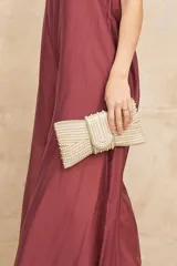 Cartera tipo clutch sobre, color dorado, completamente revestida con hileras de perlas sintéticas y cuentas brillantes, formando un diseño texturizado con solapa frontal.